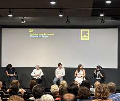 Audience looking at 5 people sitting on chairs on stage.